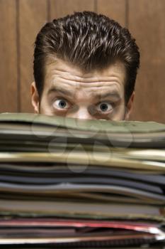 Royalty Free Photo of a Businessman Peering With Wide Eyes Over a Tall Stack of Folders