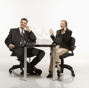Royalty Free Photo of a Businessman and Businesswoman Smiling While Sitting and Talking on Cellphones