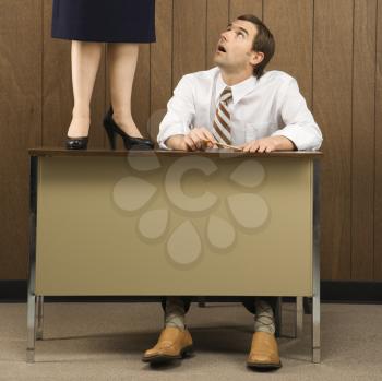 Mid-adult Caucasian male sitting at desk looking up to Caucasian female standing on desk.