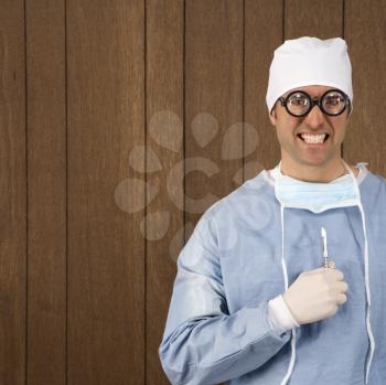 Mid-adult Caucasian male  surgeon wearing thick glasses and holding scalpel smiling maniacally.