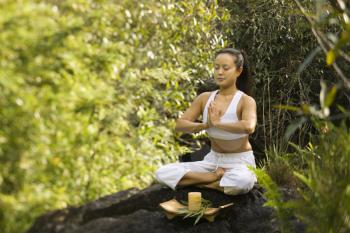 Royalty Free Photo of a Woman Sitting on a Boulder in a Forest Meditating With a Candle in Maui, Hawaii