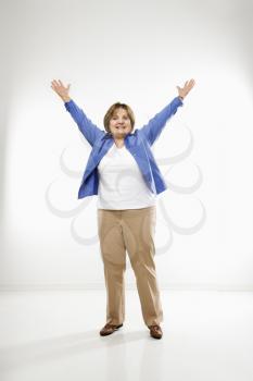 Caucasian middle aged woman standing with arms in the air smiling at viewer.