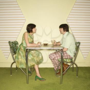 Caucasian mid-adult man and woman wearing vintage clothing sitting at 50's retro dinette set facing each other.
