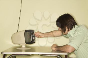 Royalty Free Photo of a Man Sitting at a 50's Retro Dinette Set Turning an Old Television Knob