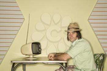 Royalty Free Photo of a Man Wearing a Hat Sitting at a 50's Retro Dinette Set in Front of a Retro Television
