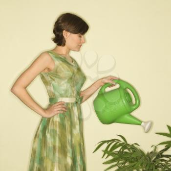 Royalty Free Photo of a Woman Wearing a Vintage Dress Watering a Houseplant With a Green Watering Can