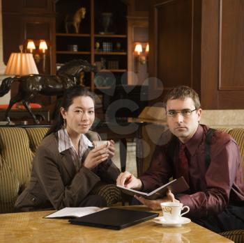 Royalty Free Photo of a Businessman and Businesswoman Drinking Coffee and Looking at a Portfolio
