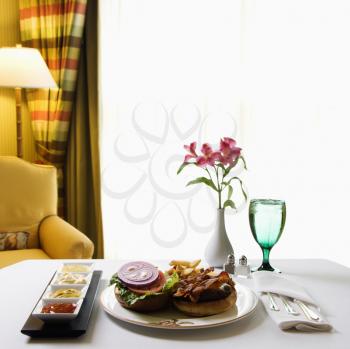 Royalty Free Photo of a Room Service Cheeseburger Meal With Flowers and Condiments