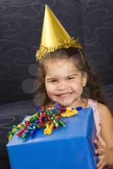 Royalty Free Photo of a Girl Wearing a Party Hat Holding a Birthday Present and Smiling