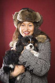 Royalty Free Photo of a Woman Wearing a Fur Hat Holding King Charles Spaniel in Her Arms and Smiling