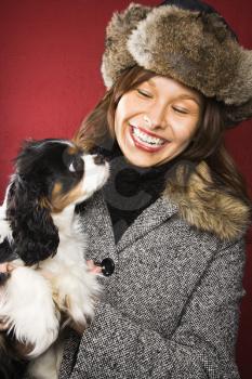 Royalty Free Photo of a Woman Wearing a Fur Hat Holding King Charles Spaniel in Her Arms and Smiling