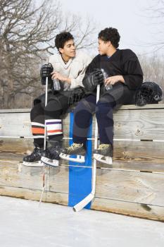 Royalty Free Photo of Two Boys in Ice Hockey Uniforms Sitting on the Sideline Talking
