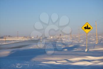 Snow covered road with snowmobile crossing sign.