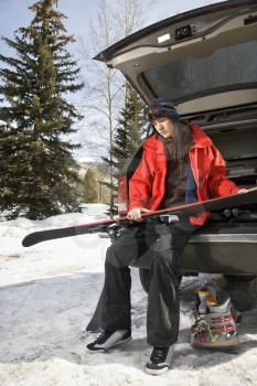 Royalty Free Photo of a Male Teenager Sitting on the Back of an SUV Holding Skis
