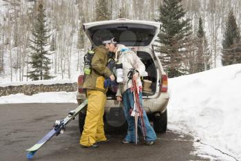 Royalty Free Photo of a Young Couple Standing by a Vehicle With Ski Equipment Kissing