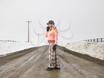 Royalty Free Photo of a Young Woman in Winter Clothes Standing on a Muddy Dirt Road Talking on a Cellphone