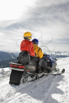 Royalty Free Photo of a Man and Woman Riding on a Snowmobile in Snowy Mountainous Terrain