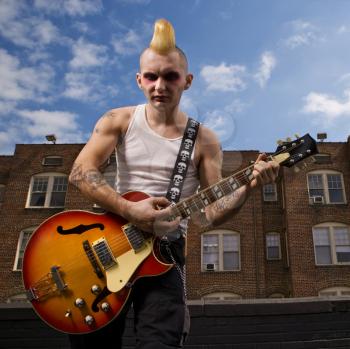 Royalty Free Photo of a Punk Playing Guitar With a Building in the Background