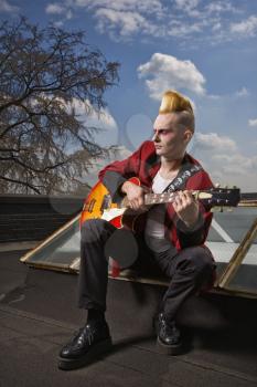 Royalty Free Photo of a Male Punk Playing Guitar With a Building in the Background