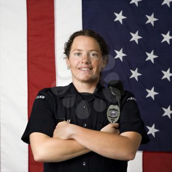Royalty Free Photo of a Policewoman Standing With Arms Crossed and an American Flag as a Backdrop
