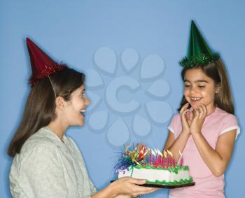 Royalty Free Photo of a Girl Wearing a Party Hat With Mother Holding a Birthday Cake