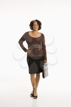 Full length portrait of businesswoman standing with hand on hip holding briefcase.