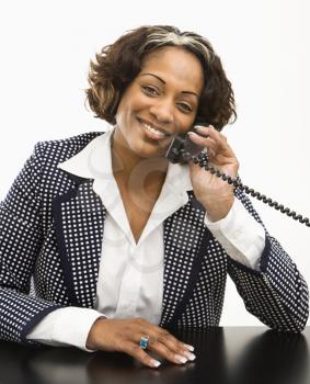 Royalty Free Photo of Businesswoman Sitting at a Desk Holding the Telephone Receiver to Her Ear Smiling