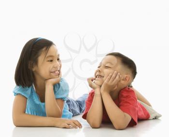 Royalty Free Photo of a Brother and Sister Lying on the Floor With Head on Hands Looking at Each Other Smiling