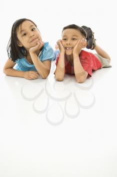 Asian brother and sister lying on floor with heads on hands.