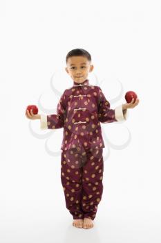 Asian boy in traditional attire standing with red apple in each hand.