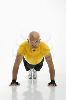 Mid adult multiethnic man wearing yellow exercise shirt doing pushups while looking at viewer.