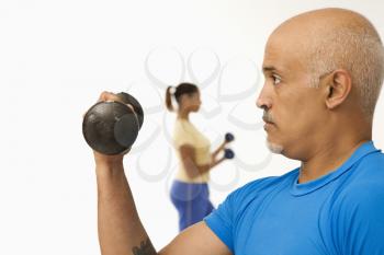 Royalty Free Photo of a Man Exercising Using Dumbbells With a Woman in the Background