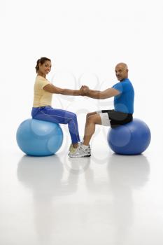 Royalty Free Photo of a Man and Woman Balancing on Blue Exercise Balls Facing Each Other With Hands and Feet Locked Together