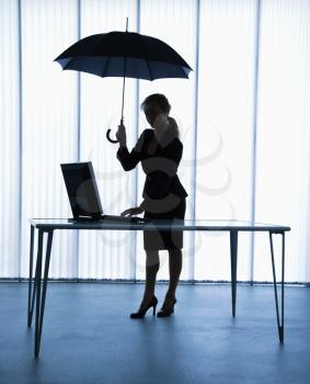 Royalty Free Photo of a Businesswoman Standing at a Computer Desk Holding an Umbrella