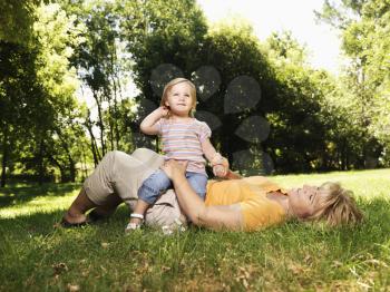 Royalty Free Photo of a Woman Lying in the Grass at a Park With Her Toddler Daughter Seated on Her Lap