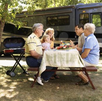 Royalty Free Photo of a Three Generation Family Seated at a Picnic Table in Front of a Recreational Vehicle