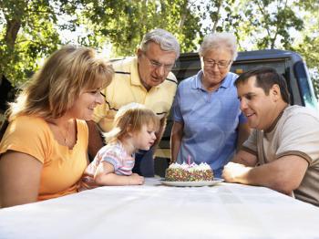 Royalty Free Photo of a Family Seated at a Picnic Table Celebrating a Little Girls Birthday With a Cake