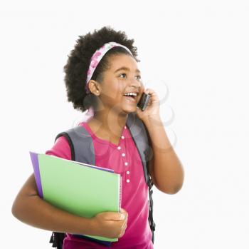 Royalty Free Photo of an African American girl With Books and Wearing a Backpack While Talking on a Cellphone