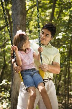 Royalty Free Photo of a Father Pushing His Daughter on a Swing and Smiling