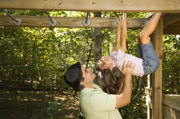 Royalty Free Photo of a Girl Hanging by Arms and Legs From Monkey Bars With her Father Helping