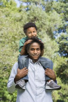 Royalty Free Photo of a Father Carrying His Son on His Shoulders in a Park