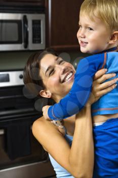 Royalty Free Photo of a woman in kitchen lifting smiling toddler son into the air