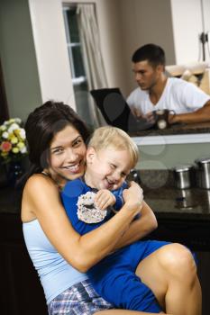 Royalty Free Photo of a Mother Hugging Her Son With a Man on a Laptop in the Background