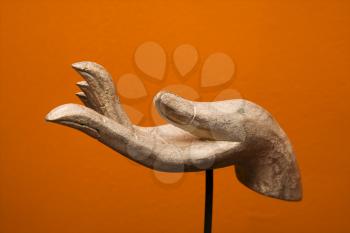 Royalty Free Photo of a Carved Hand Sculpture from Thailand Against Orange Wall