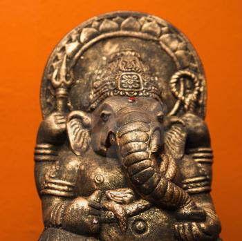 Statue of Hindu elephant Ganesha against orange wall.