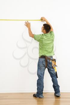 Royalty Free Photo of a Man Wearing a Tool Belt Measuring an Interior Wall