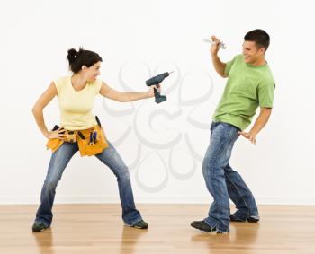 Royalty Free Photo of a Woman Pointing a Drill Playfully at a Man Smiling