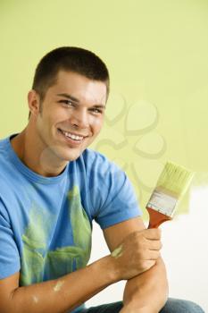 Royalty Free Photo of a Man Kneeling in Front of a Partially Painted Wall Holding a Paintbrush
