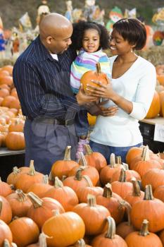 Royalty Free Photo of Parents and Their Daughter Picking Out a Pumpkin and Smiling at an Outdoor Market