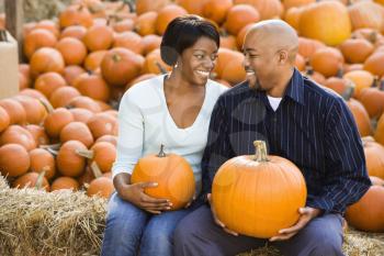 Royalty Free Photo of a Smiling Couple Sitting on Hay Bales and Holding Pumpkins at an Outdoor Market